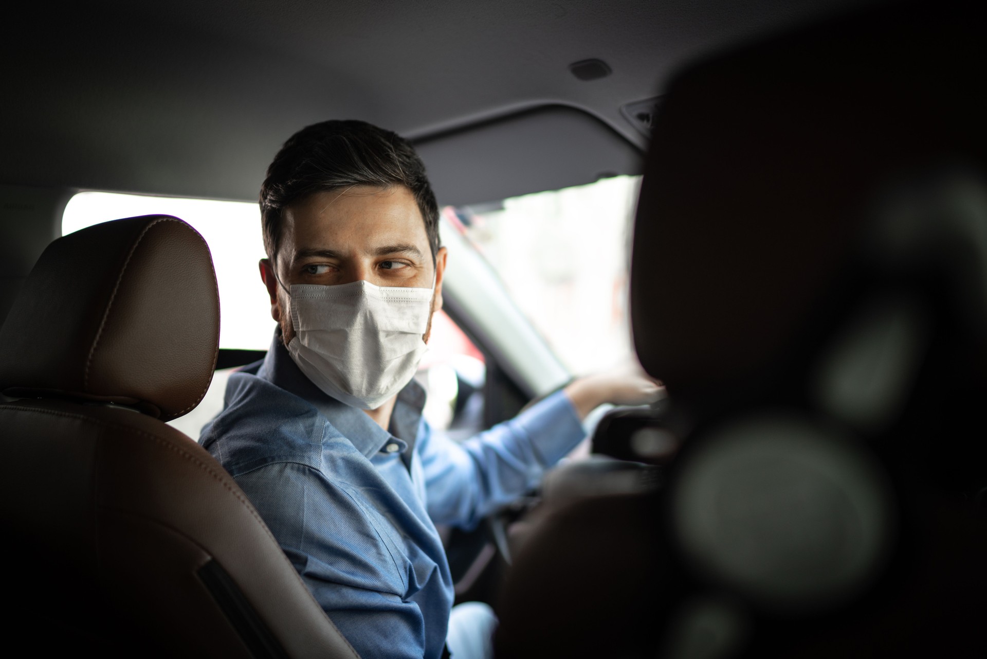 Driver taking to a passenger on seat back wearing protective medical mask