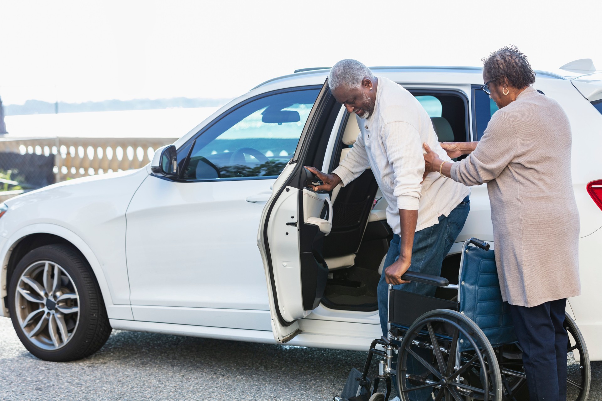 Senior man exiting car into wheelchair, wife helping